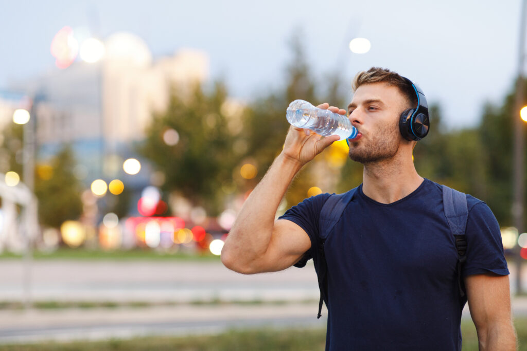 man drinking water wearing headphones outdoors